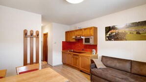 A modern kitchen with wooden cabinets, a red backsplash, and a microwave. There is a dining table with chairs and a brown leather sofa. - Holiday Apartment "Casa Marcos n 31" with Mountain View, Balcony & Wi-Fi (Livigno)