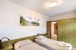 Une chambre avec deux lits, une table de chevet, une lampe, un tableau au mur et une armoire.
