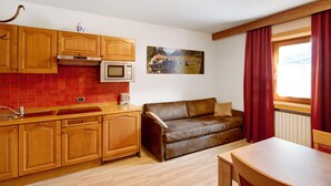 A kitchen with wooden cabinets, a red-tiled backsplash, a microwave, and a window with red curtains. - Holiday Apartment "Casa Marcos n 31" with Mountain View, Balcony & Wi-Fi (Livigno)