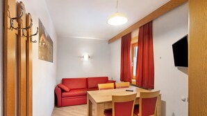 Une pièce avec une table à manger en bois, des chaises rouges, un canapé rouge, un tableau accroché au mur et un téléviseur fixé au mur.