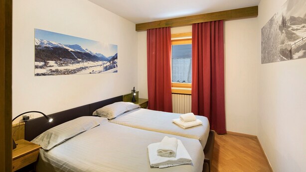 Une chambre d’hôtel avec deux lits, une table de chevet, une lampe et une fenêtre avec des rideaux rouges.