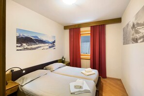 Een hotelkamer met twee bedden, een nachtkastje, een lamp en een raam met rode gordijnen.
