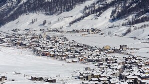 Un village enneigé, avec des maisons et une montagne en arrière-plan.