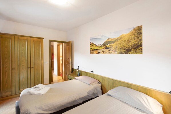 A bedroom with two beds, a wardrobe, a painting, and a door leading to another room.