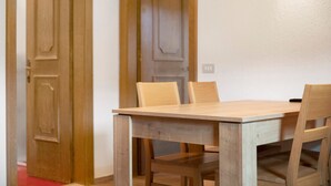 A wooden dining table with chairs, a red carpet, and wooden doors in the background. - Holiday Apartment "Casa Marcos n 32" with Mountain View, Balcony & Wi-Fi (Livigno)