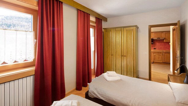 A bedroom with two beds, a window with curtains, a wooden wardrobe, and a view of a kitchen. - Holiday Apartment "Casa Marcos n 32" with Mountain View, Balcony & Wi-Fi (Livigno)