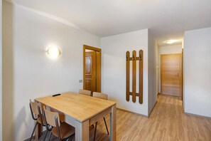 A dining area with a wooden table and chairs, a wall-mounted light, and a wooden door.
