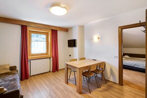 A room with a wooden table, chairs, a TV, a bed, and a window with curtains.