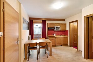 Une cuisine de taille réduite avec des meubles de rangement en bois, une table à manger avec des chaises et un rideau rouge.