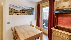 A kitchen with a wooden table, chairs, a red-tiled backsplash, a window with a view, and a mounted picture of a landscape. - Holiday Apartment "Casa Marcos n 36" with Mountain View, Balcony & Wi-Fi (Livigno)