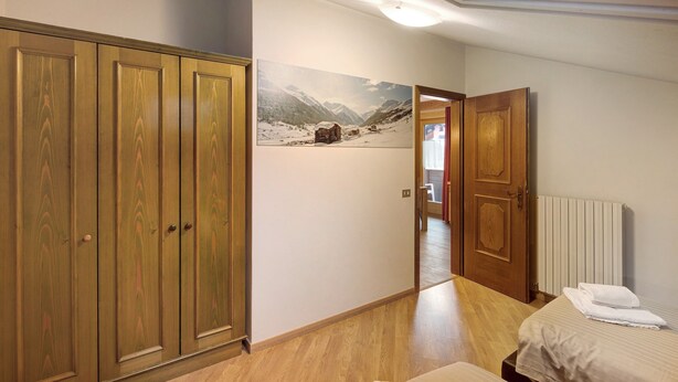 A bedroom with a bed, a wooden wardrobe, a radiator, and a painting on the wall. - Holiday Apartment "Casa Marcos n 36" with Mountain View, Balcony & Wi-Fi (Livigno)