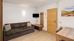 A room with a sofa, a wooden table, a TV mounted on the wall, and a door. - Holiday Apartment "Casa Marcos n 36" with Mountain View, Balcony & Wi-Fi (Livigno)