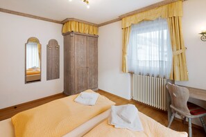 Quarto com duas camas, guarda-roupa de madeira, radiador, uma cadeira e um espelho.