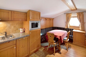 A compact kitchen with wooden cabinets, a microwave, a sink, and a dining area with a table and chairs.