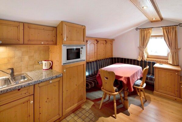 A compact kitchen with wooden cabinets, a microwave, a sink, and a dining area with a table and chairs.