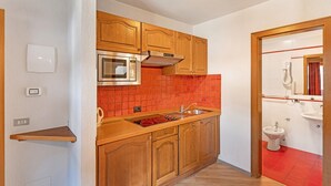 A compact kitchen with wooden cabinets, a built-in microwave, and a red-tiled backsplash. - Holiday Apartment "Casa Marcos n 33" with Mountain View, Balcony & Wi-Fi (Livigno)
