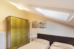 A bedroom with a skylight, a bed with two pillows, a nightstand, and a wardrobe.