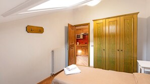 A bedroom with a bed, a wooden wardrobe, a small table, and a view into a kitchen. - Holiday Apartment "Casa Marcos n 33" with Mountain View, Balcony & Wi-Fi (Livigno)