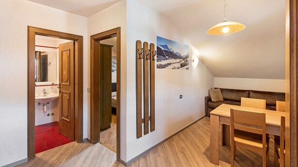 A room with a wooden dining table, a brown sofa, a ceiling light, and a wall-mounted picture. - Holiday Apartment "Casa Marcos n 33" with Mountain View, Balcony & Wi-Fi (Livigno)