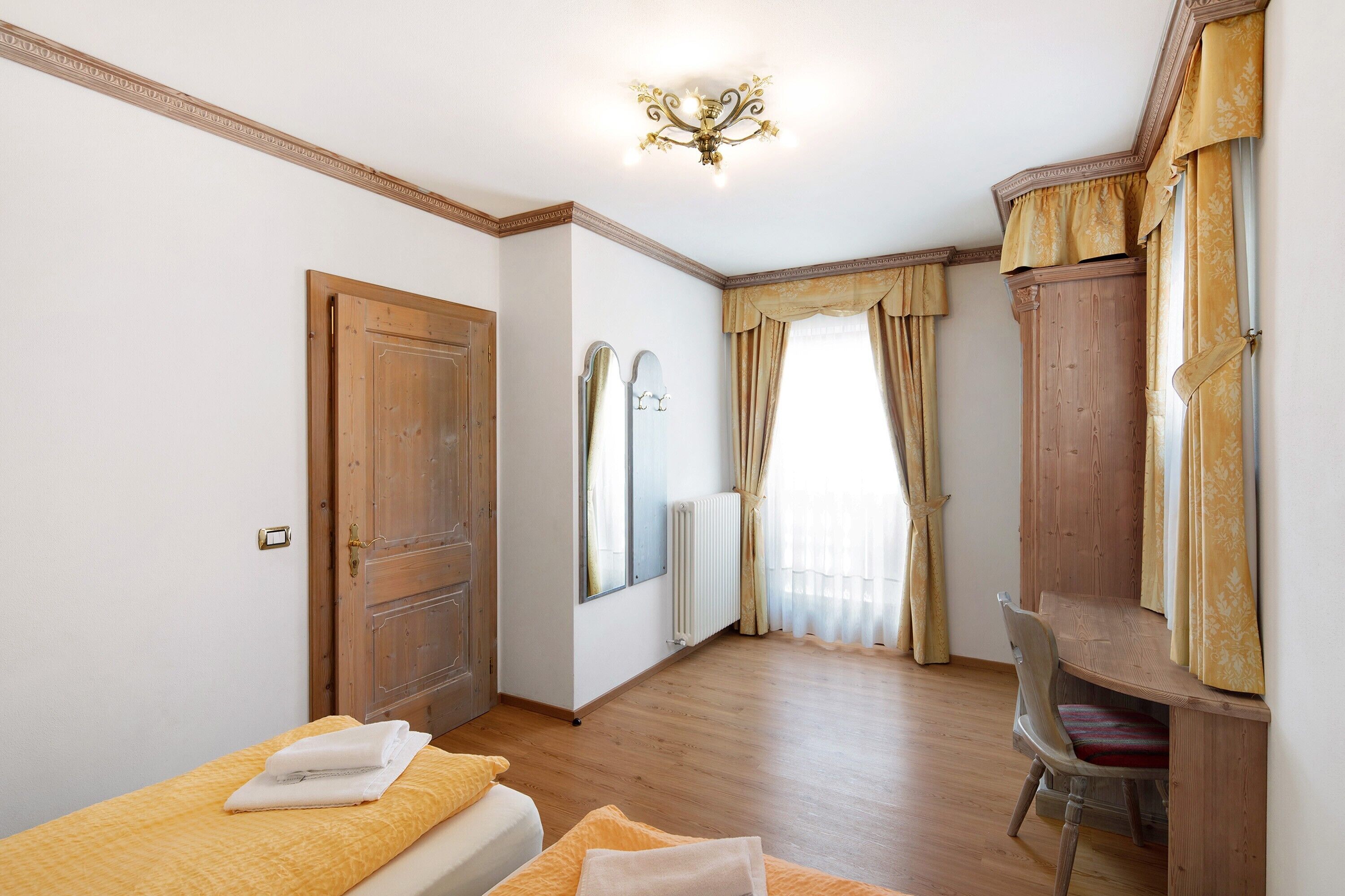 A bedroom with a wooden bed, a desk, a chair, a wardrobe, and a mirror.