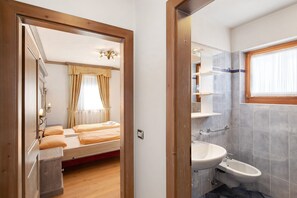 A room with a bed, a bedside table, a mirror, and a window with curtains.