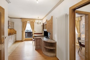 A room with a wooden desk, a television, a radiator, and a view of the outside.