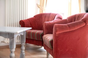 A red armchair with a striped cushion, a wooden table, and a radiator in the background.