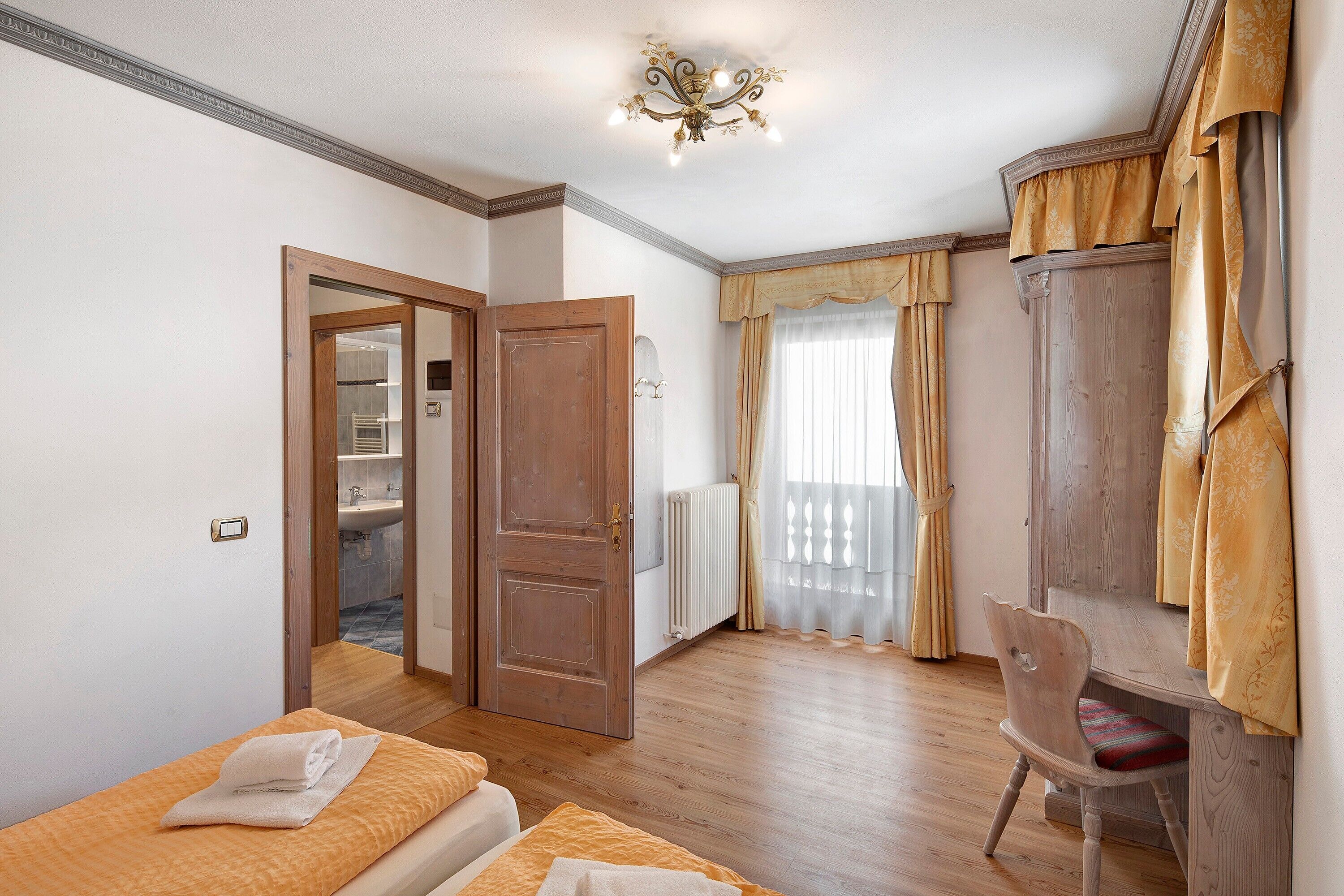 A bedroom with a bed, a chair, a wardrobe, and a bathroom visible through an open door.