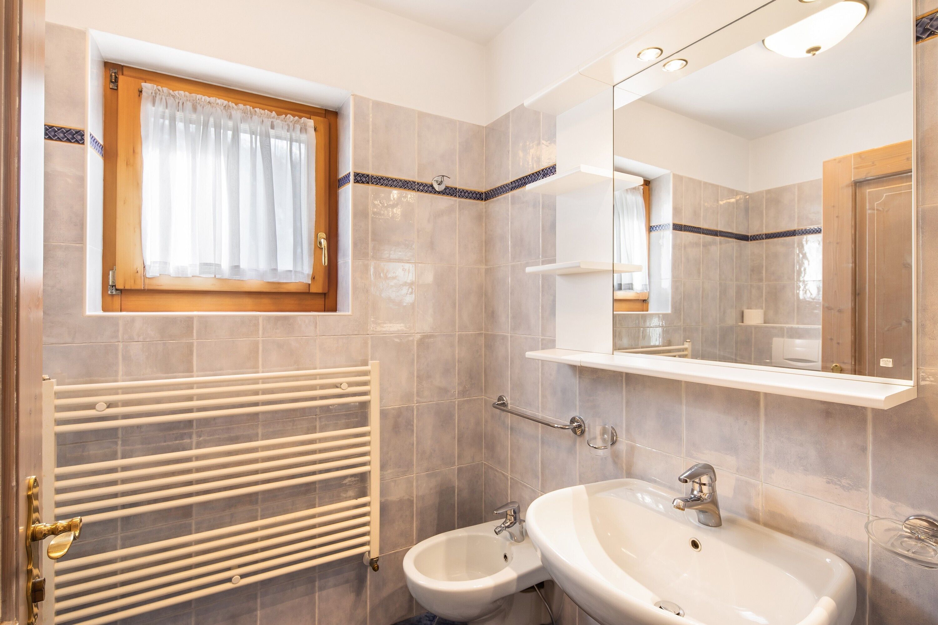 A bathroom with a bidet, a sink, a mirror, and a window with a curtain.