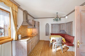 Une cuisine avec des meubles de rangement en bois, un évier et une cuisinière. On y trouve une table à manger, des chaises et un banc.