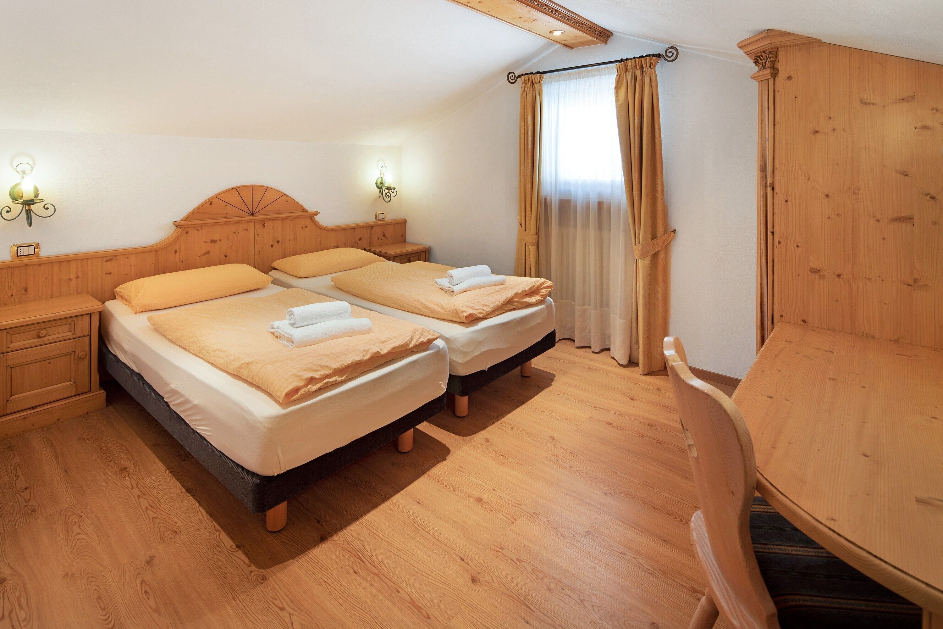 A double bed with a wooden headboard, a wooden chair, and a wooden table in a room with wooden flooring and walls.