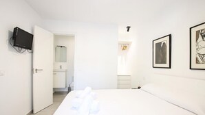 Ett hotellrum med en säng, en tv, ett badrum och inramade konstverk på väggen.