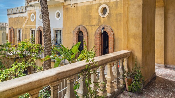 A courtyard with a stone balustrade, a palm tree, and buildings with arched doorways. - Apartment 'Casa Florio' with Shared Terrace, Wi-Fi and Air Conditioning (Taormina)