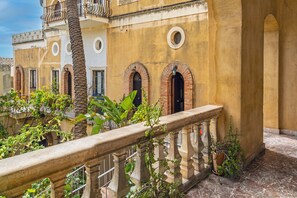 A courtyard with a stone balustrade, a palm tree, and buildings with arched doorways. - Apartment 'Casa Florio' with Shared Terrace, Wi-Fi and Air Conditioning (Taormina)