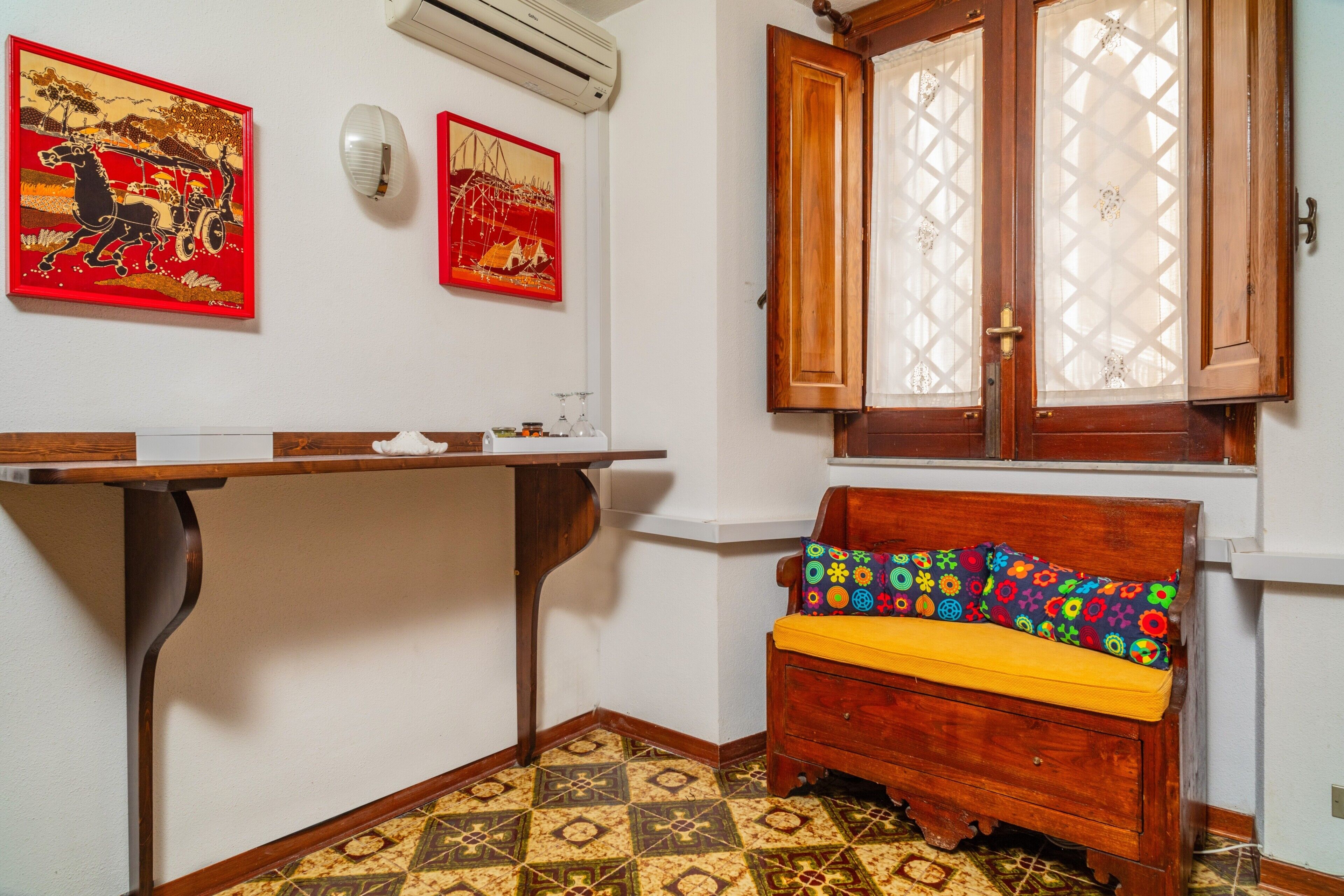 A room with a wooden bench, a table, two wall-mounted air conditioning units, and patterned floor tiles.