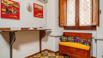 A room with a wooden bench, a table, two wall-mounted air conditioning units, and patterned floor tiles.