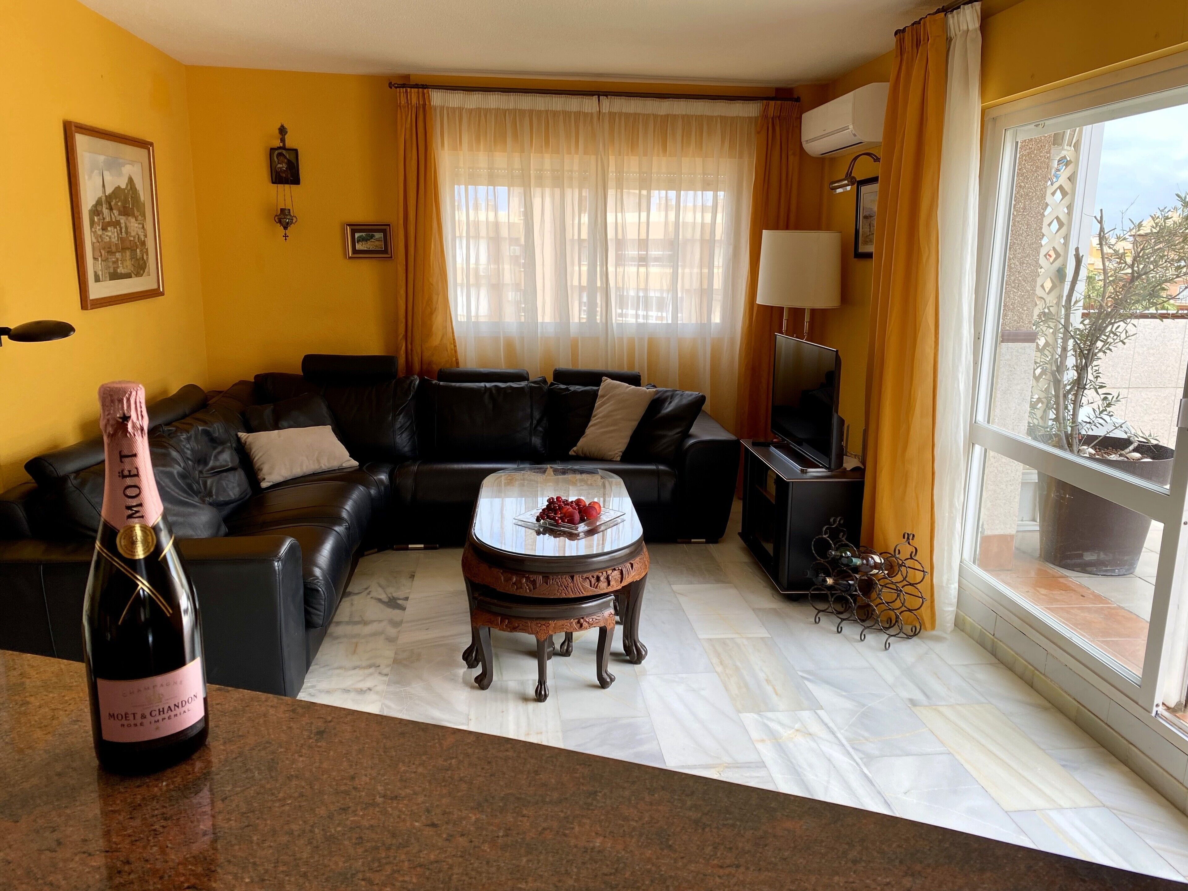 A living room with a sofa, a glass coffee table, a bottle of champagne, and a television.