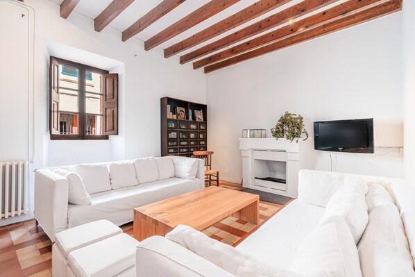 Una sala de estar con un sofá blanco, una mesa de centro de madera, una chimenea y un televisor montado en la pared.