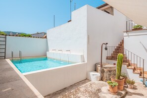 Una piscina en la azotea con agua azul cristalina, una pared blanca y una planta de cactus.