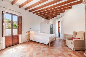 Un dormitorio con cama, una silla, una mesita de noche, una ventana con cortinas y un radiador.
