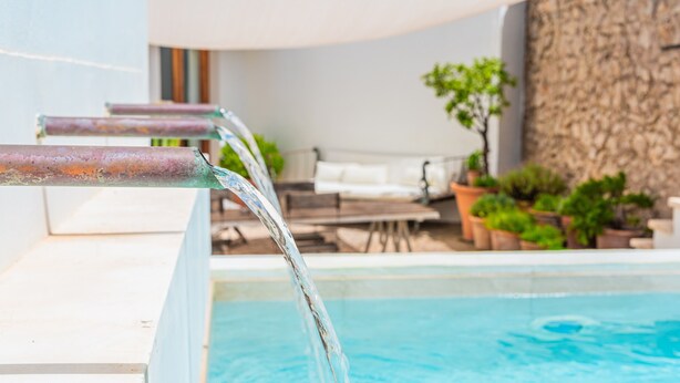 En pool med vatten som rinner in i den, omgiven av ett område med bekväma sittplatser och krukväxter.