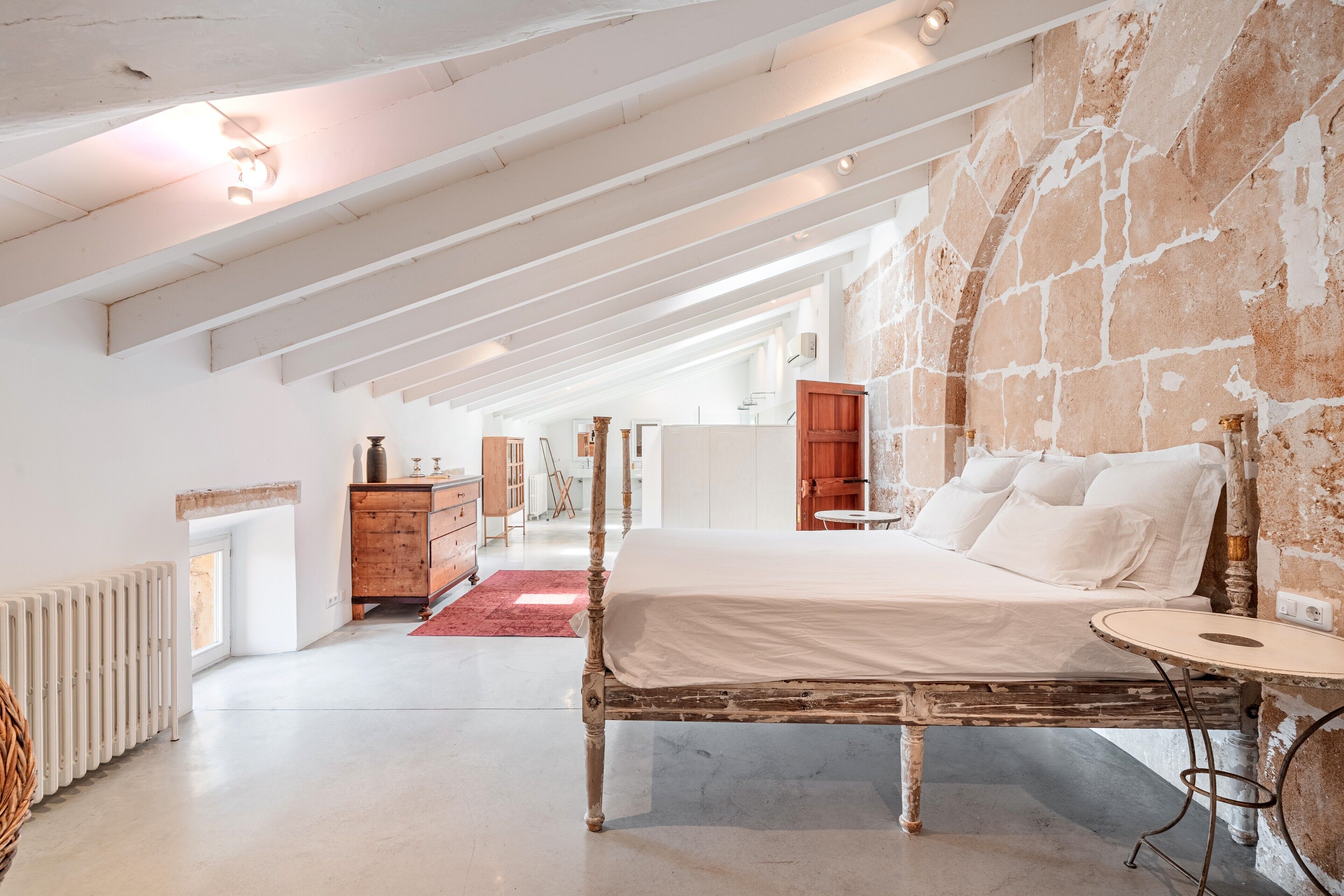 Un dormitorio con una cama grande, un aparador de madera, una alfombra roja y una pared de piedra.