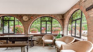 Ein Zimmer mit Steinböden, Bogenfenstern, Korbmöbeln und Topfpflanzen.