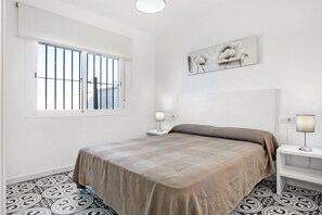 Een slaapkamer met een bed, een raam met tralies, een aan de muur hangend kunstwerk en een kamer met een patroon vloer.