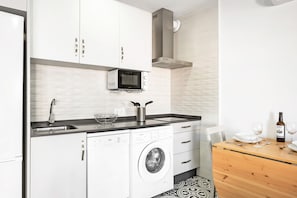 A compact kitchen with a washing machine, a microwave, a sink, and a dining area with a table and chairs.