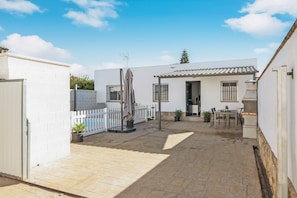A courtyard with a white building, a white fence, a patio area, and a table with chairs.