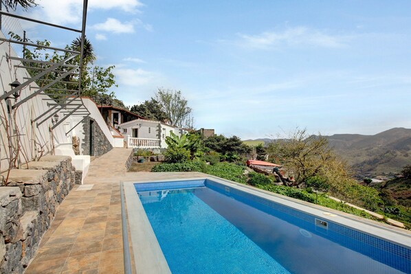 A swimming pool with stone steps leading up to a house, surrounded by greenery and hills.