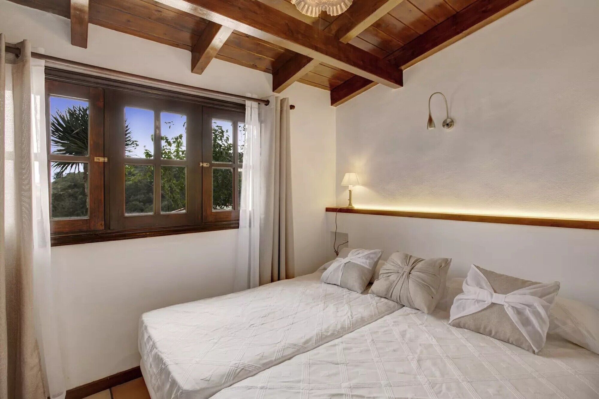 Un dormitorio con cama, ventana y lámpara fijada a la pared.