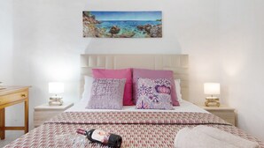 A bedroom with a bed, two bedside tables, a nightstand, a lamp, and a painting of a coastal scene. - Holiday Home "Faro de Sardina Frente al Mar" with Sea View, Pool & Wi-Fi (Galdár)