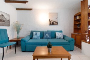 Un salon avec un canapé de couleur turquoise, une table basse en bois, une bibliothèque et un tableau encadré accroché au mur.